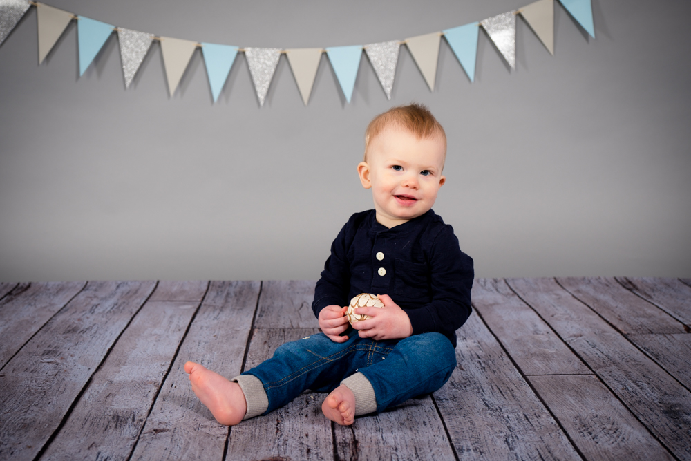 Little boy sitting and smiling with gey backdrops