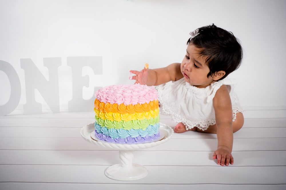 Little girl touching her rainbow cake.